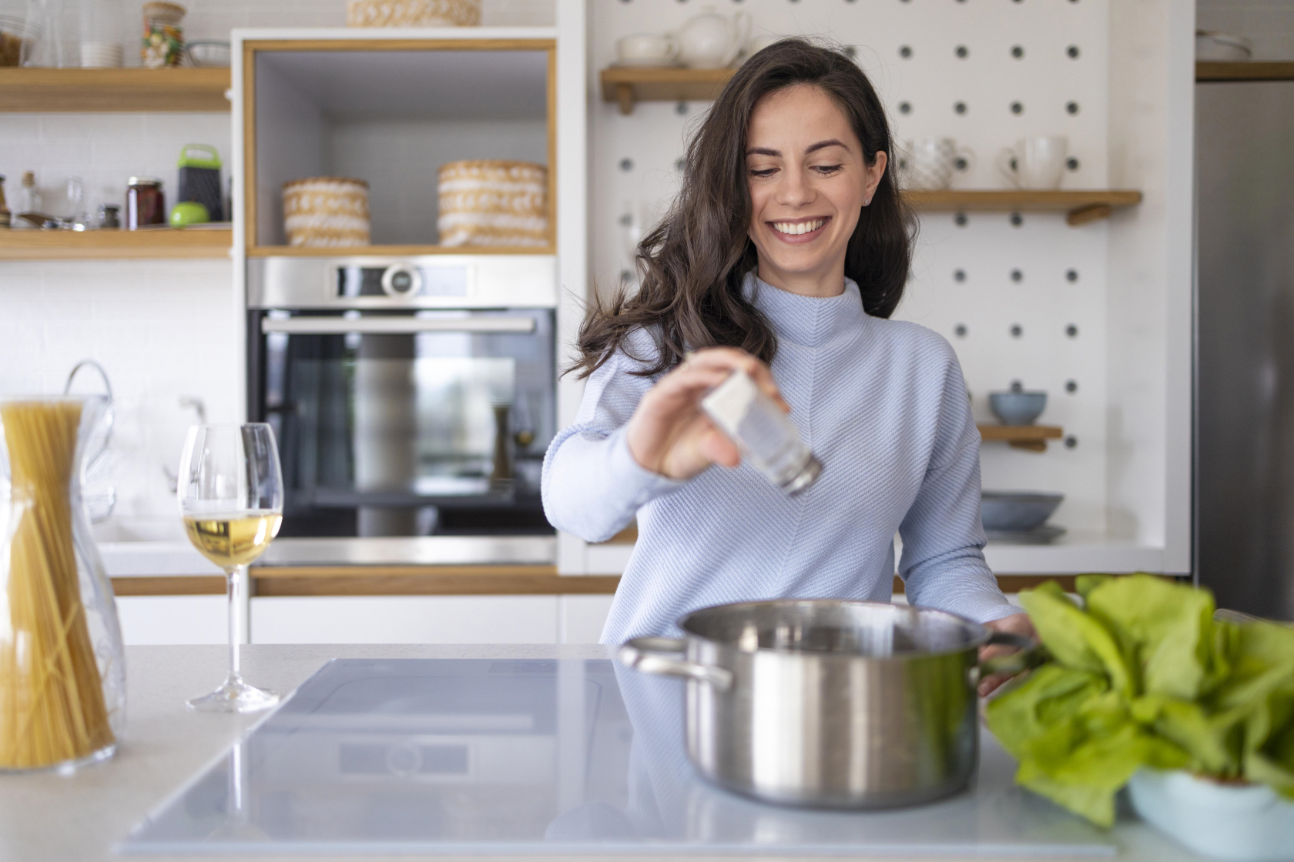 Una mujer feliz cocinando echándole sal a una cacerola