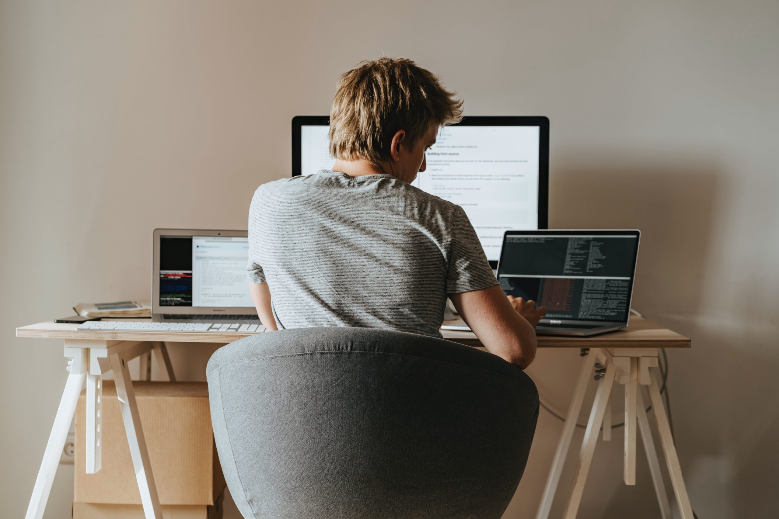 Hombre trabajando desde casa en su escritorio con tres pantallas diferentes